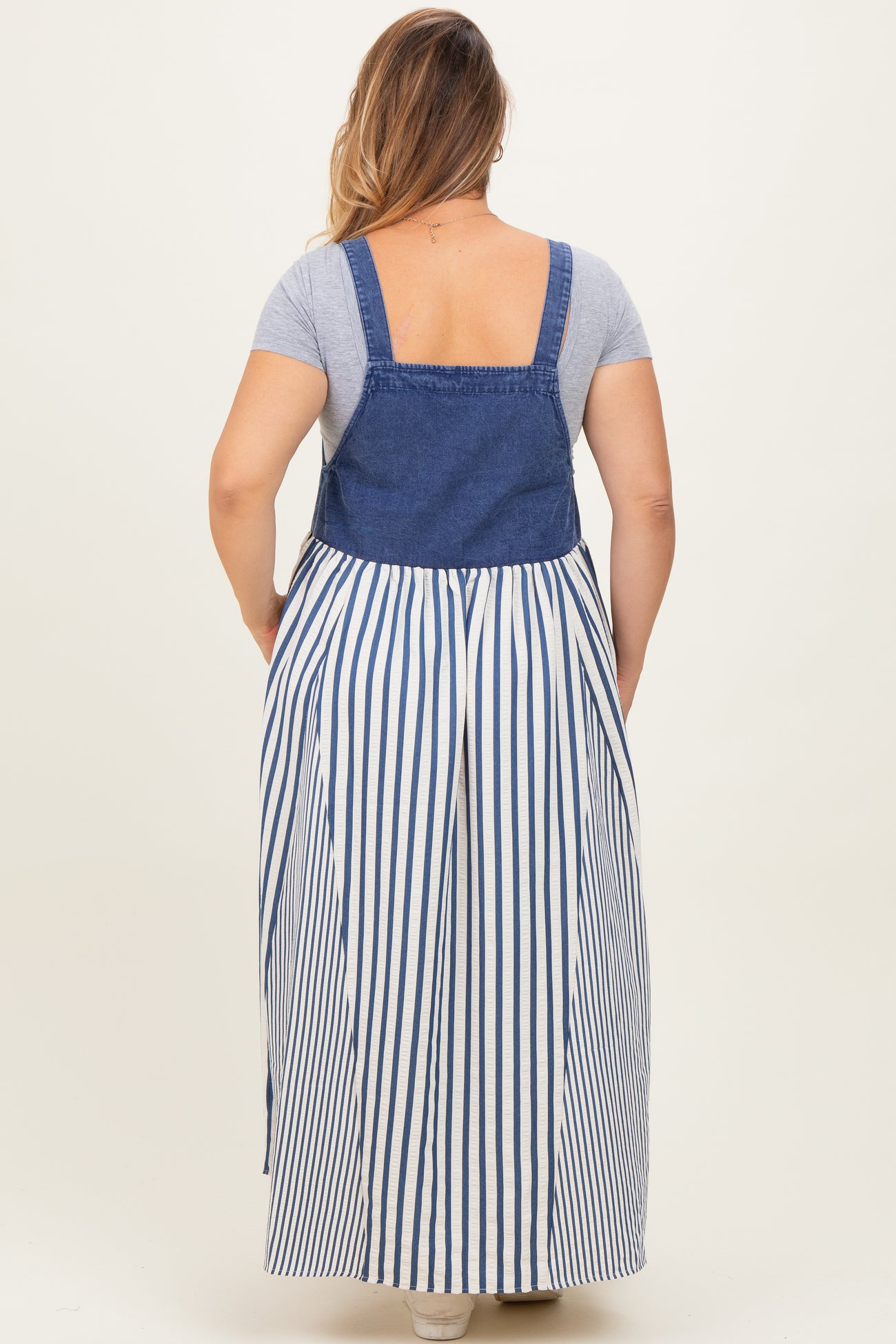 woman wearing a blue denim and white striped maternity plus maxi dress with a fitted top and loose skirt from the back