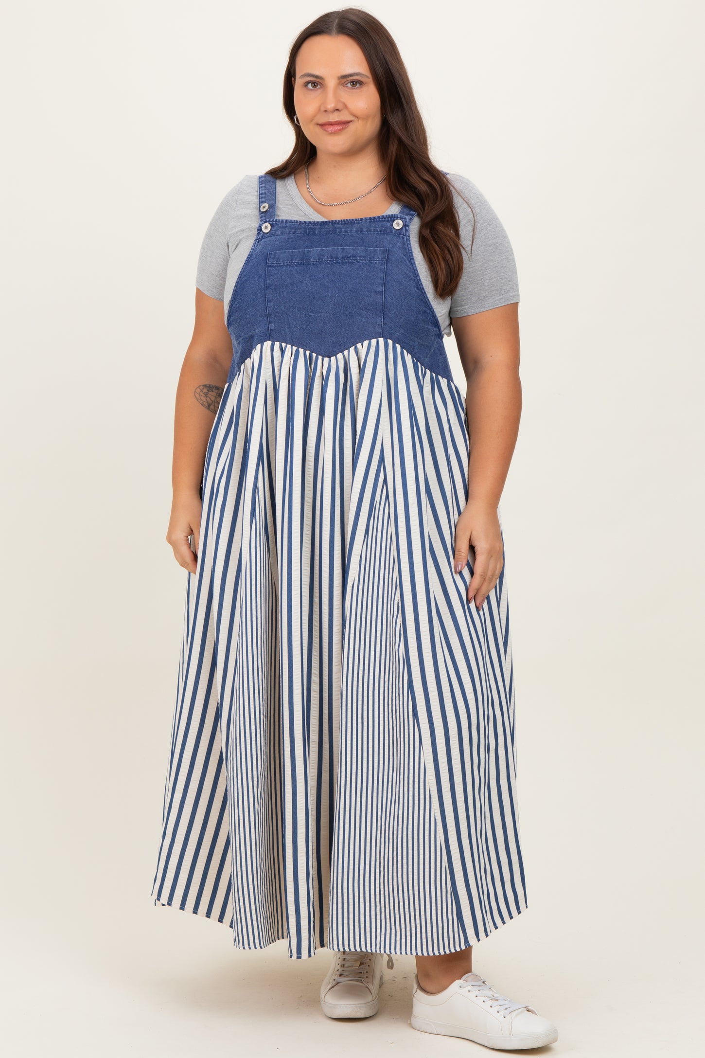 woman wearing a denim and striped plus size midi dress styled with a fitted gray t-shirt underneath