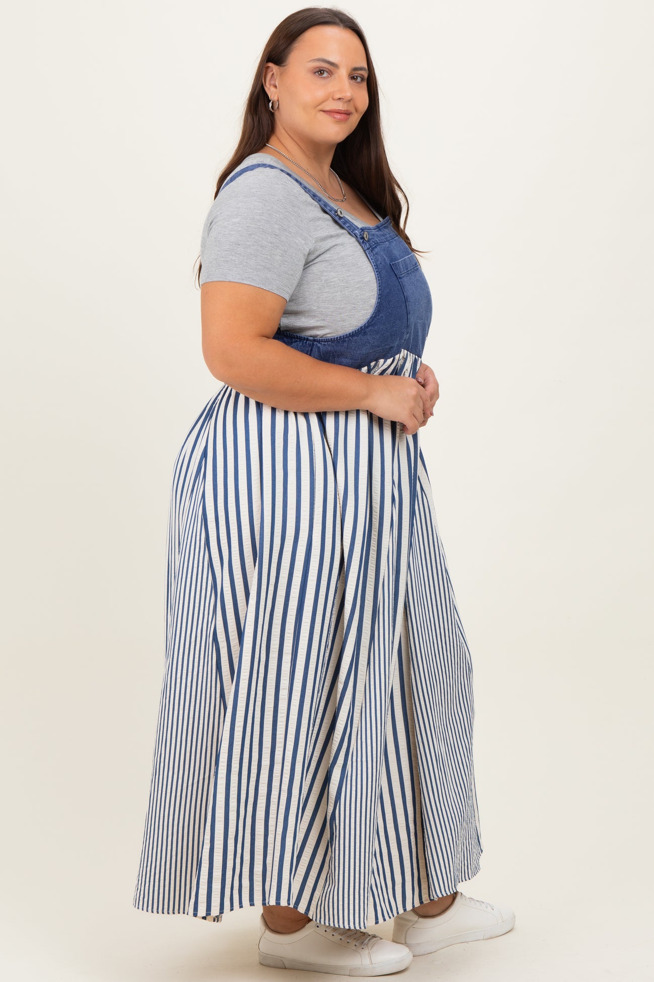 woman wearing a striped maxi dress with denim overalls and a gray t-shirt underneath