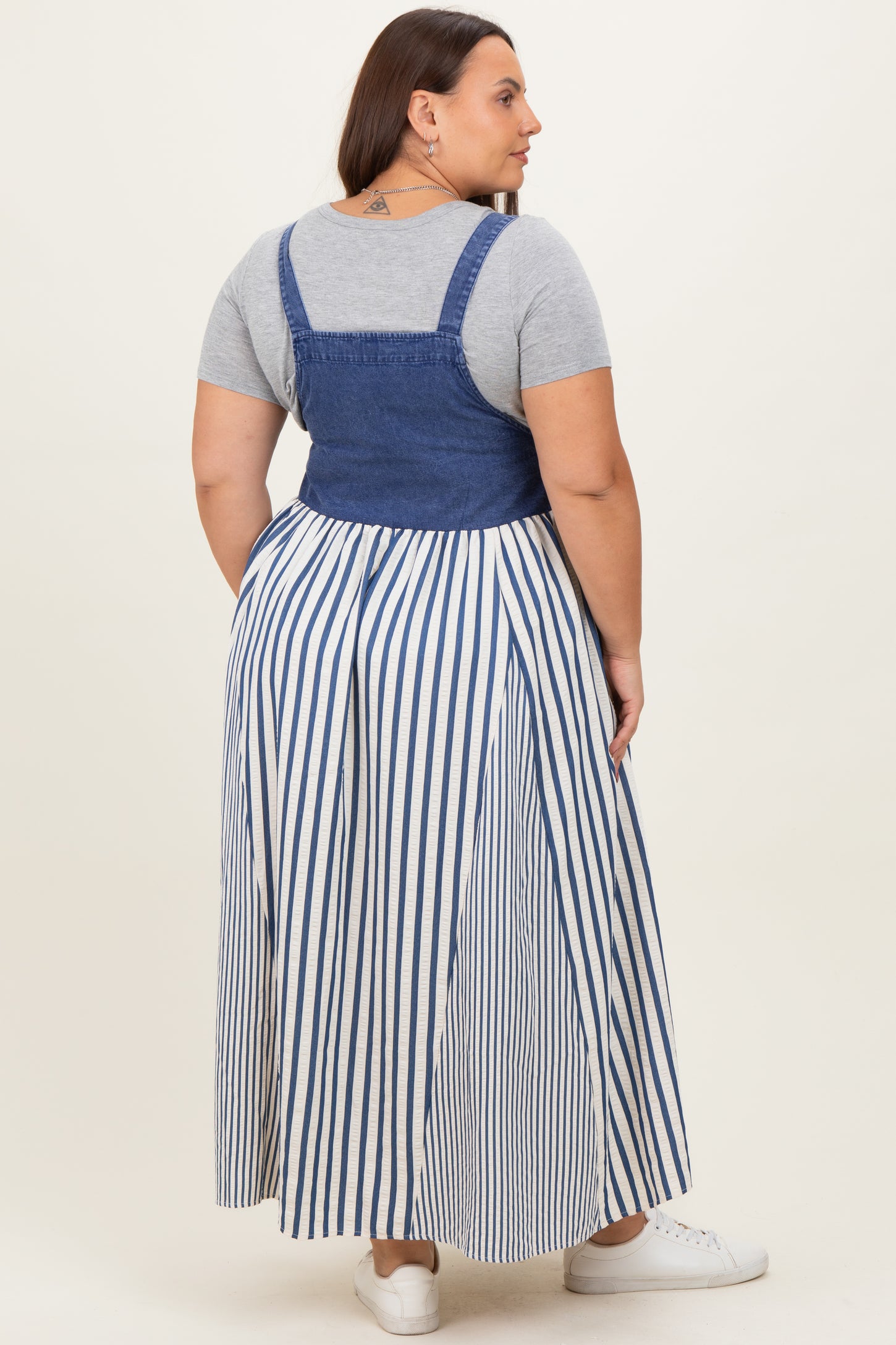 woman wearing a gray short sleeve top with a denim bodice and a long striped skirt, viewed from the back