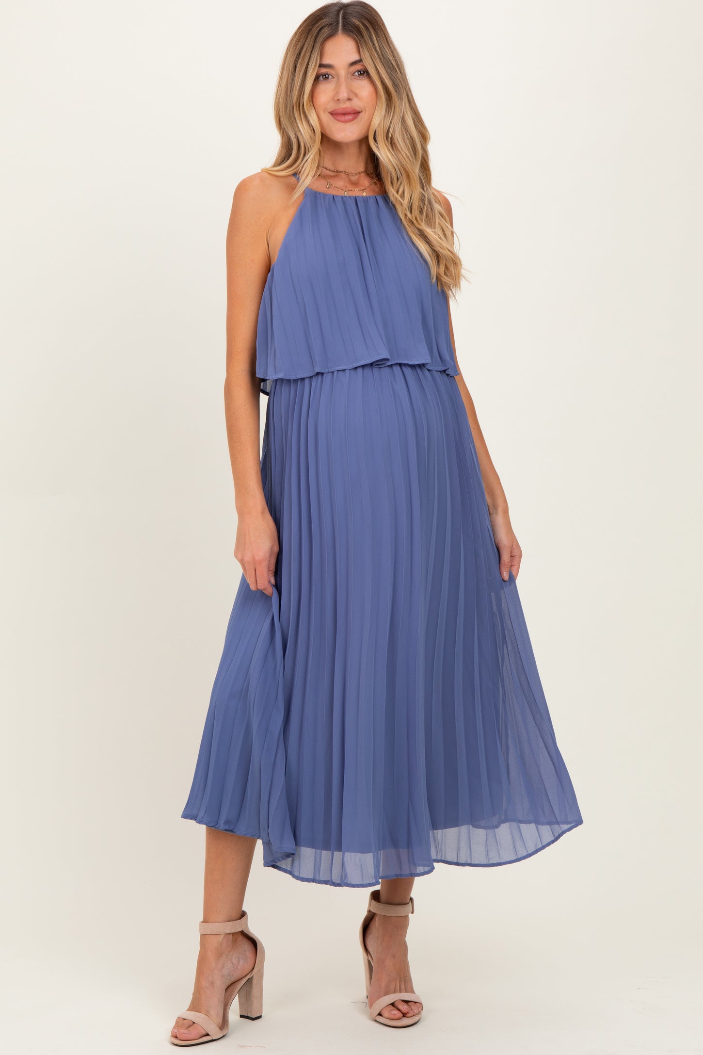 woman wearing a pleated blue maternity maxi dress with a halter neckline and flowy silhouette, showcasing her baby bump
