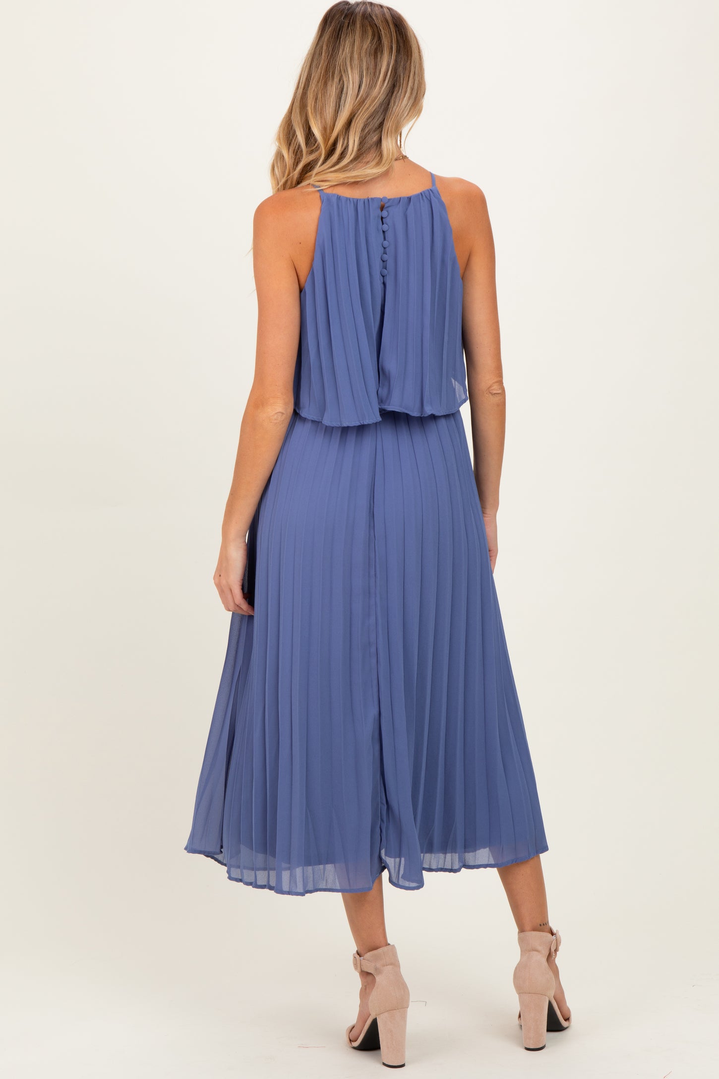 woman wearing a pleated blue maternity dress with a flowy top and a knee-length skirt, showing a baby bump from the back