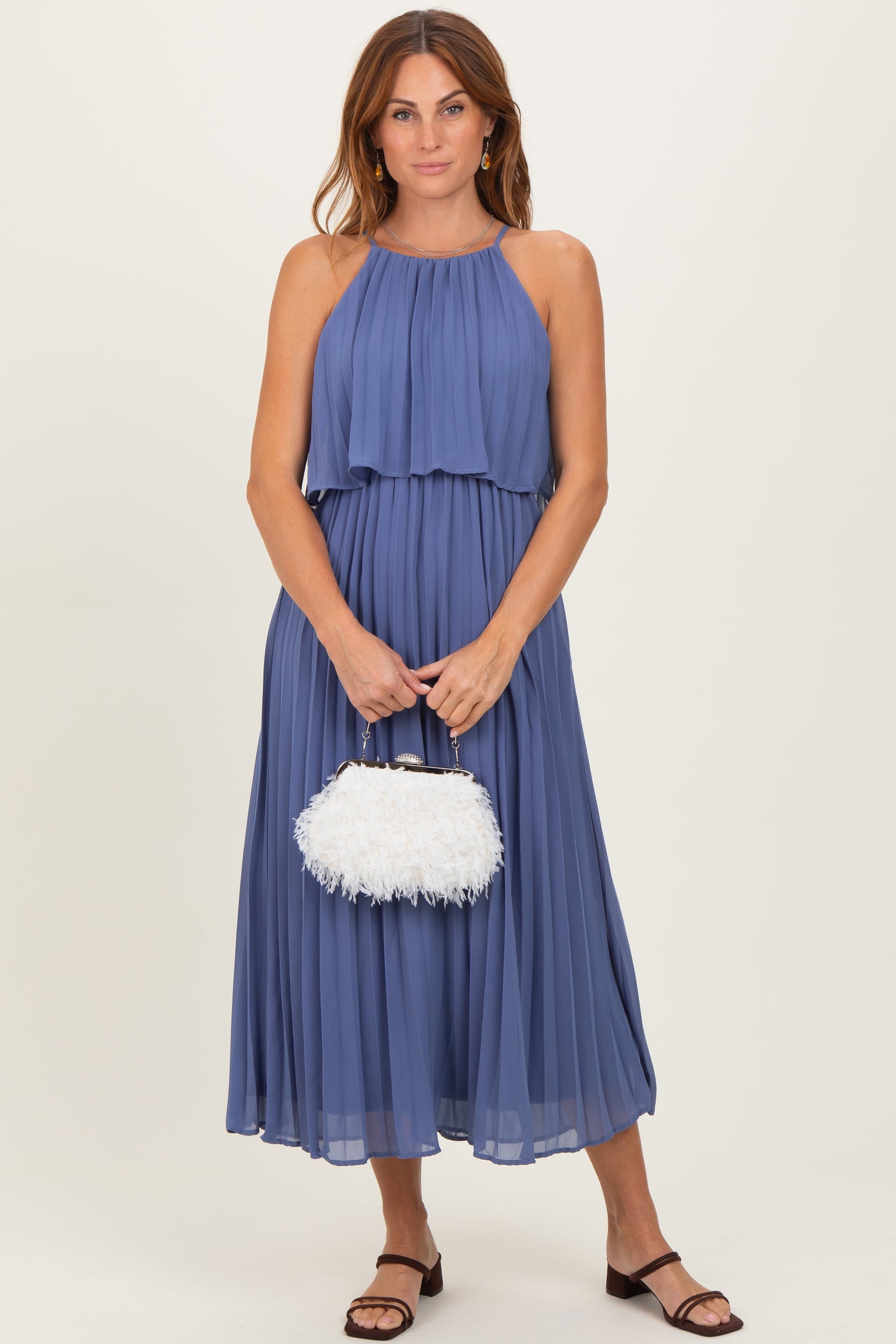 woman wearing a pleated blue maxi dress with a halter neck and a white fluffy handbag