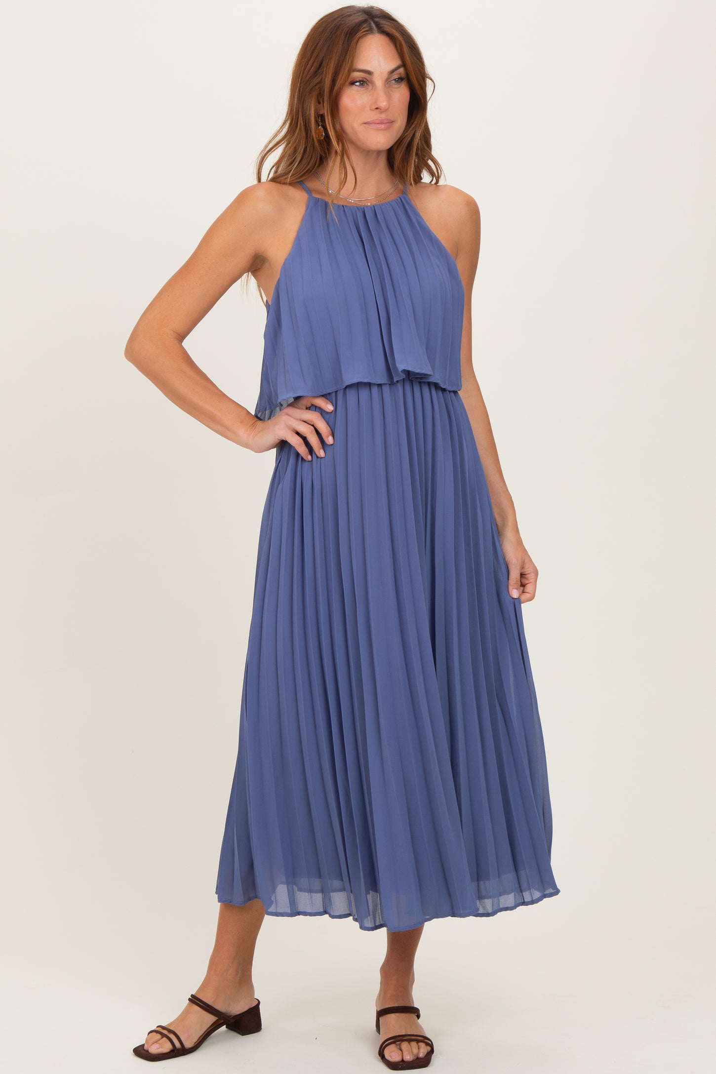 woman wearing a flowy pleated halter neck dress in light blue with a layered top and mid-length skirt