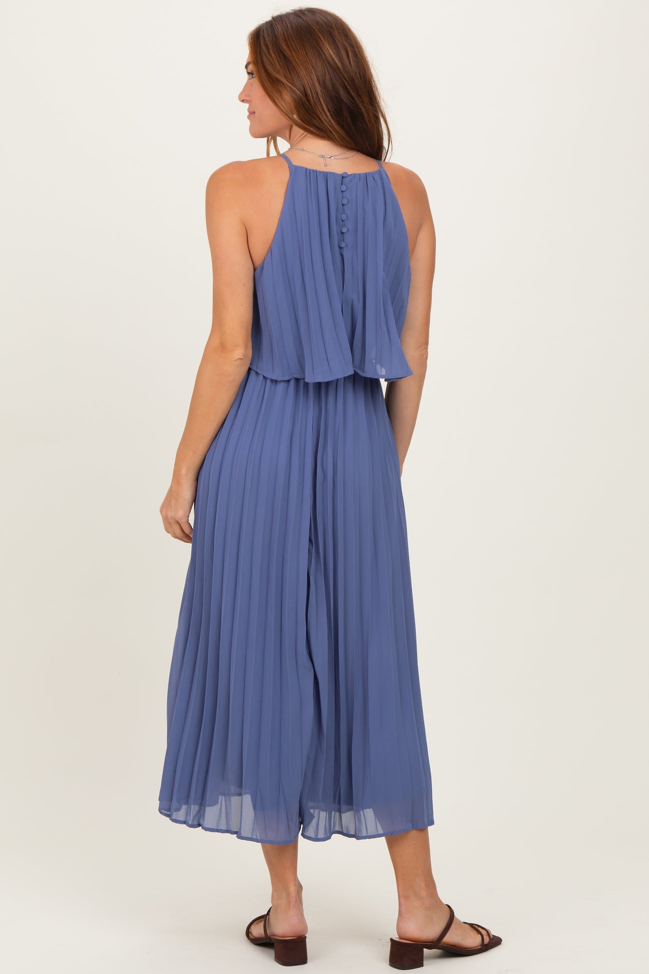 woman wearing a pleated halter neck maxi dress in a soft blue color, with a layered back detail and sandals