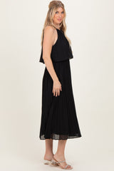 woman wearing a black pleated midi dress with layered top and a flowy silhouette, standing sideways