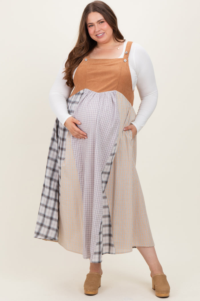 woman wearing a tan maternity plus overall dress with plaid detailing, showing her baby bump and smiling