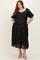 woman wearing a black puff sleeve maxi maternity dress with a textured floral design and pockets