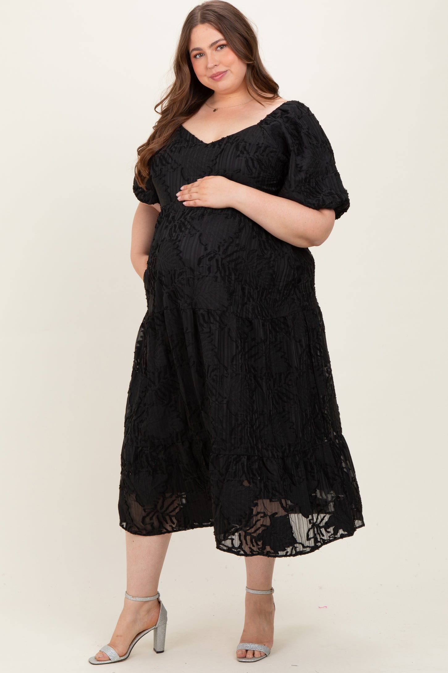 woman wearing a black maternity plus dress with floral detailing, cradling her baby bump