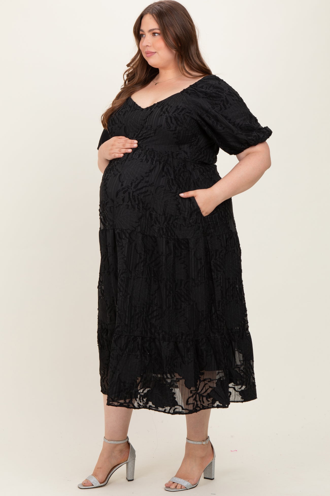 woman wearing a black floral lace maternity dress with pockets and holding her baby bump