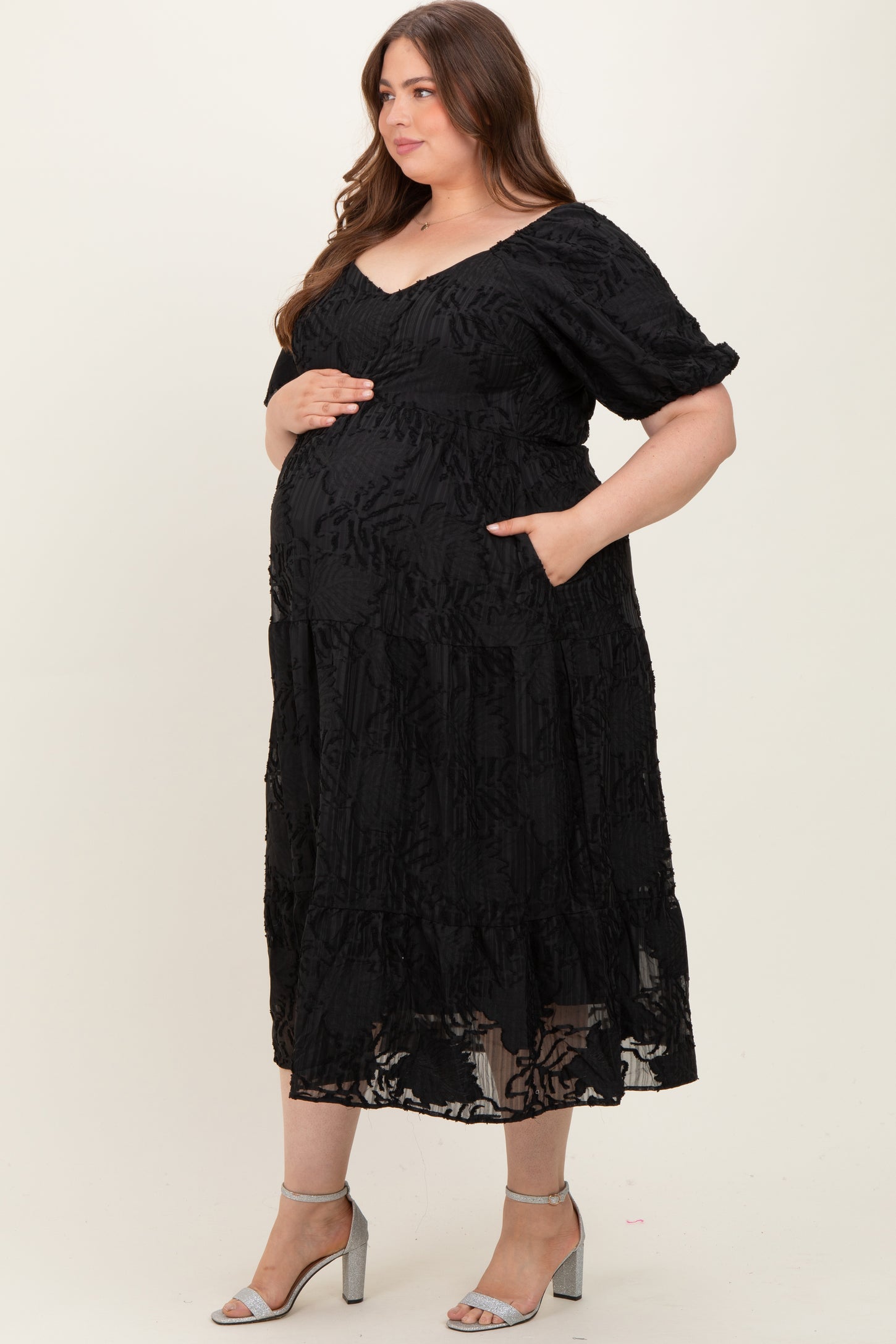 woman wearing a black floral lace maternity dress with pockets and holding her baby bump