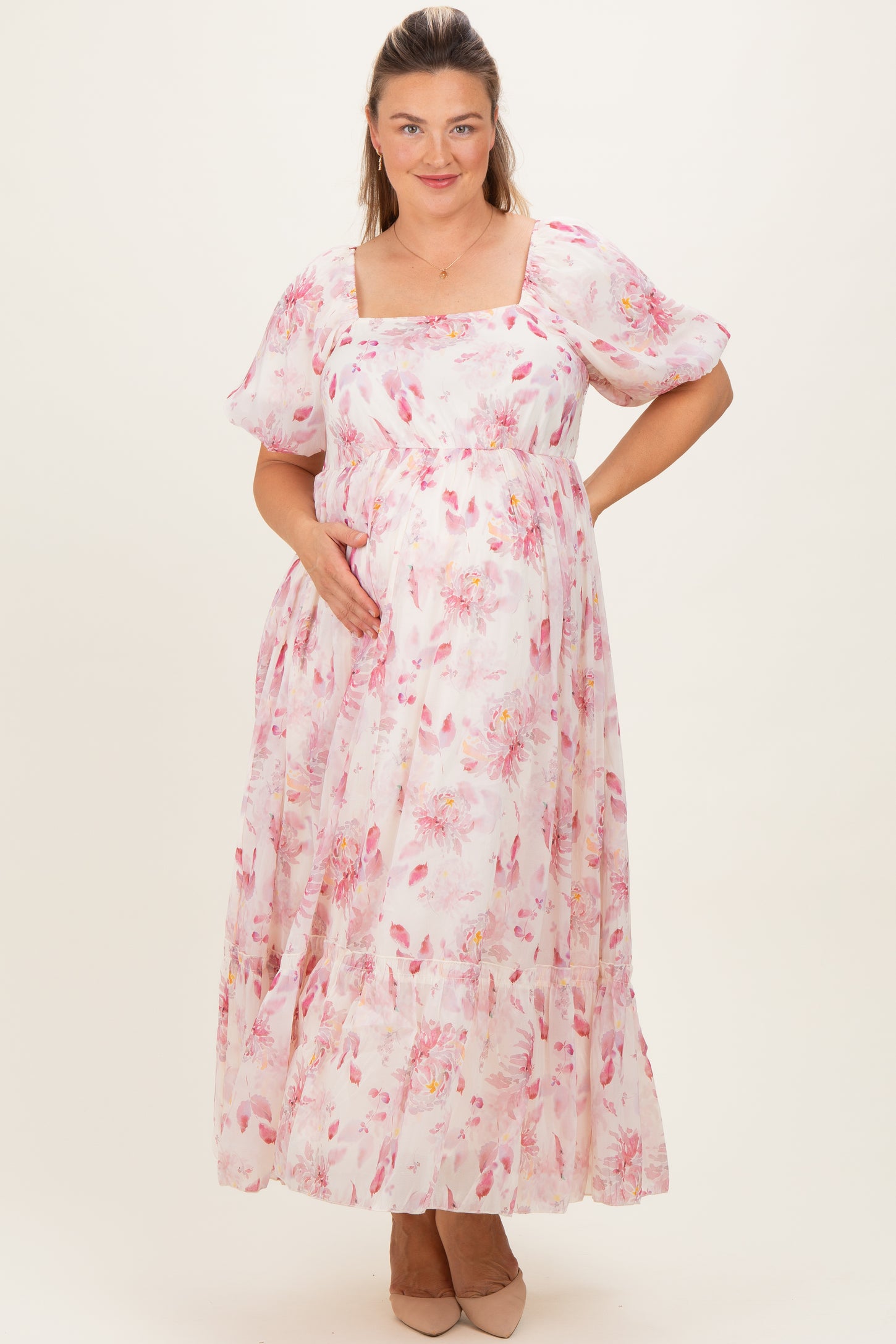 woman wearing a pink floral maternity maxi dress and gently cradling her baby bump