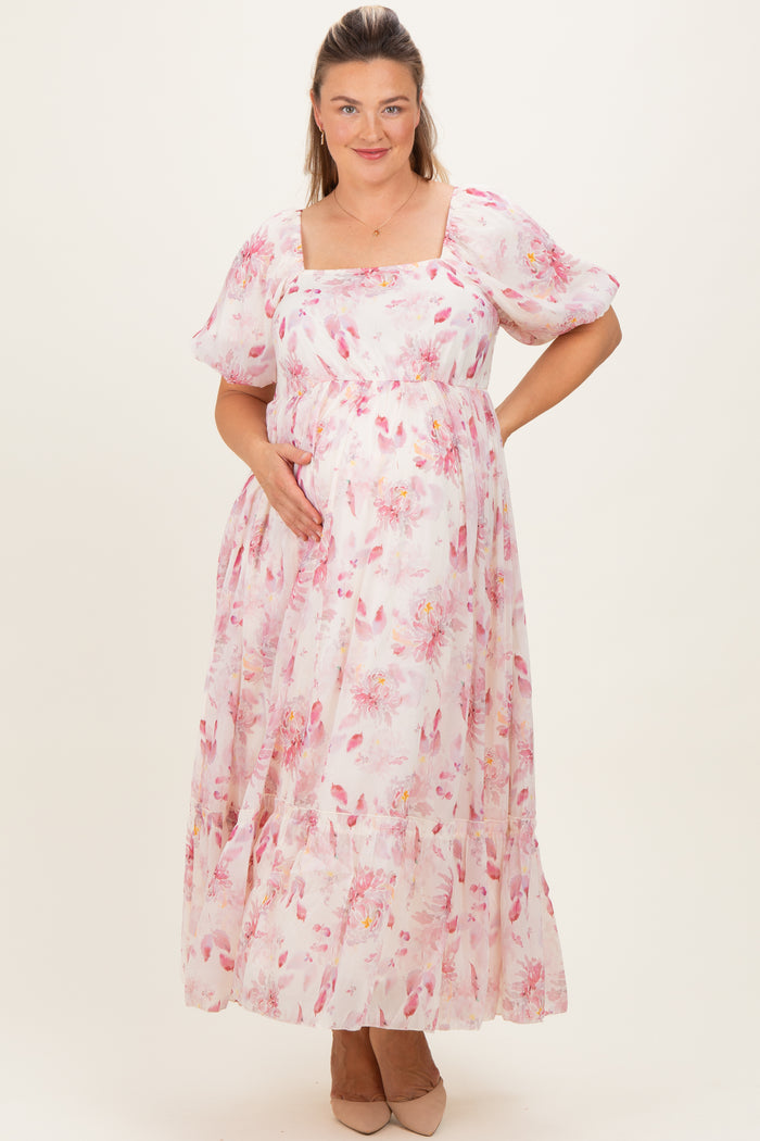 woman wearing a pink floral maternity maxi dress and gently cradling her baby bump