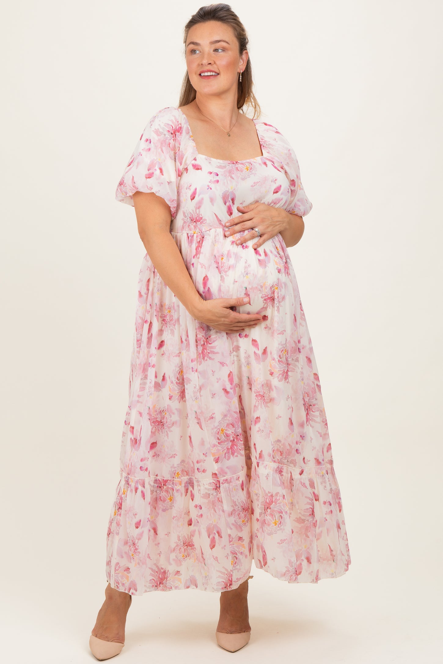 woman wearing a floral pink maternity plus maxi dress and holding her baby bump
