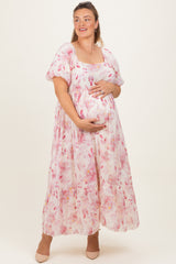 woman wearing a floral pink maternity plus maxi dress and holding her baby bump