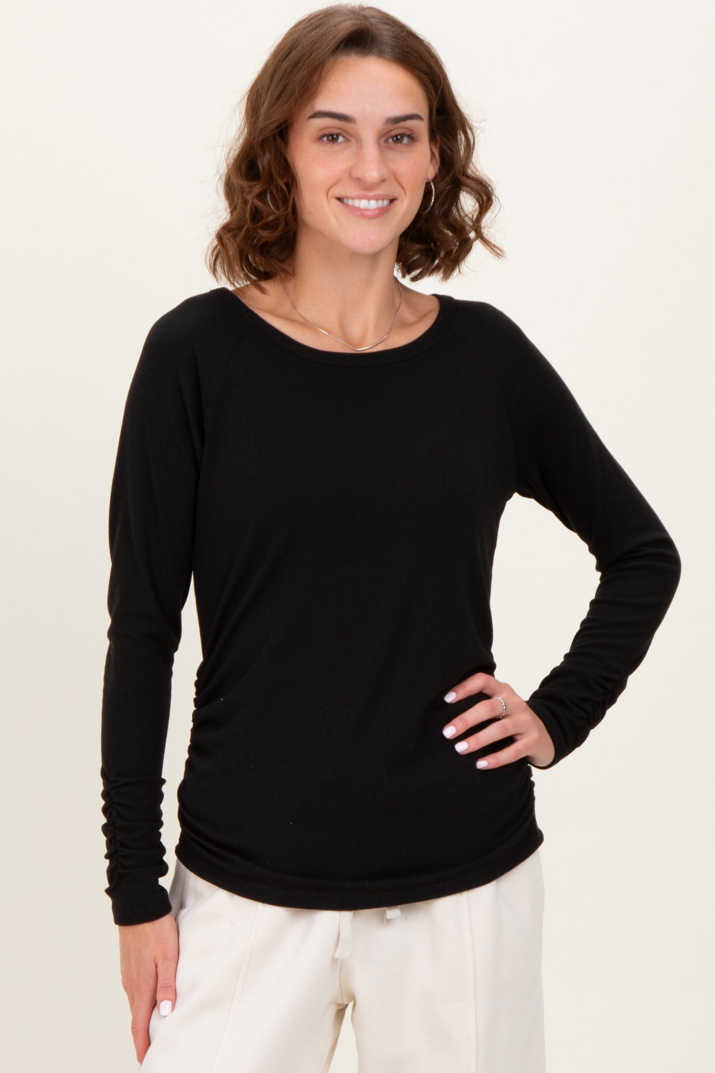 woman wearing a black long sleeve top with ruched details, smiling against a neutral background