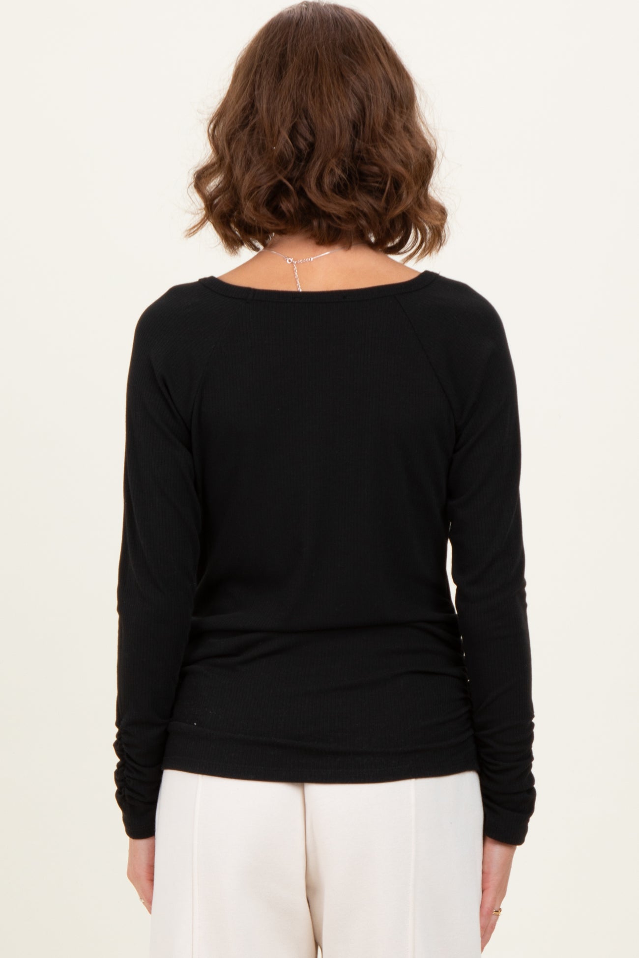 woman wearing a black long sleeve ribbed top, viewed from the back, paired with cream-colored pants