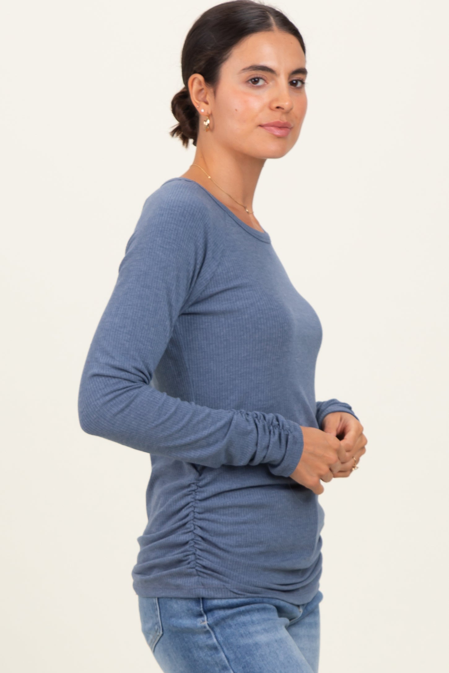woman wearing a blue long sleeve fitted top with gathered side details and paired with light wash jeans