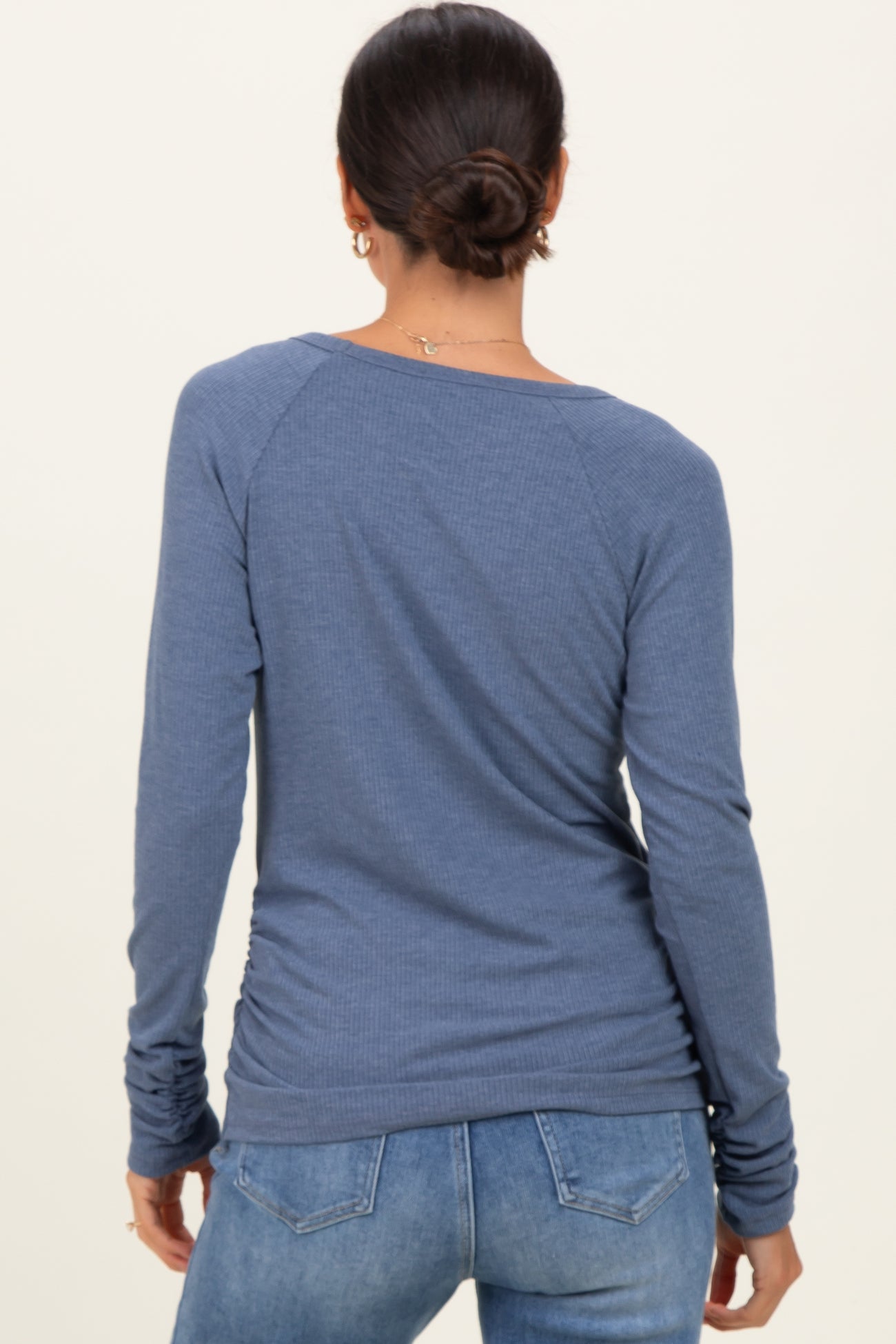 woman wearing a blue long sleeve top with a ribbed texture and gathered side detail, facing away from the camera