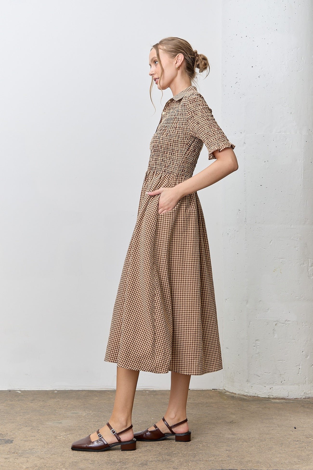 woman wearing a brown and cream checkered midi dress with a smocked bodice and pockets, styled with flat shoes