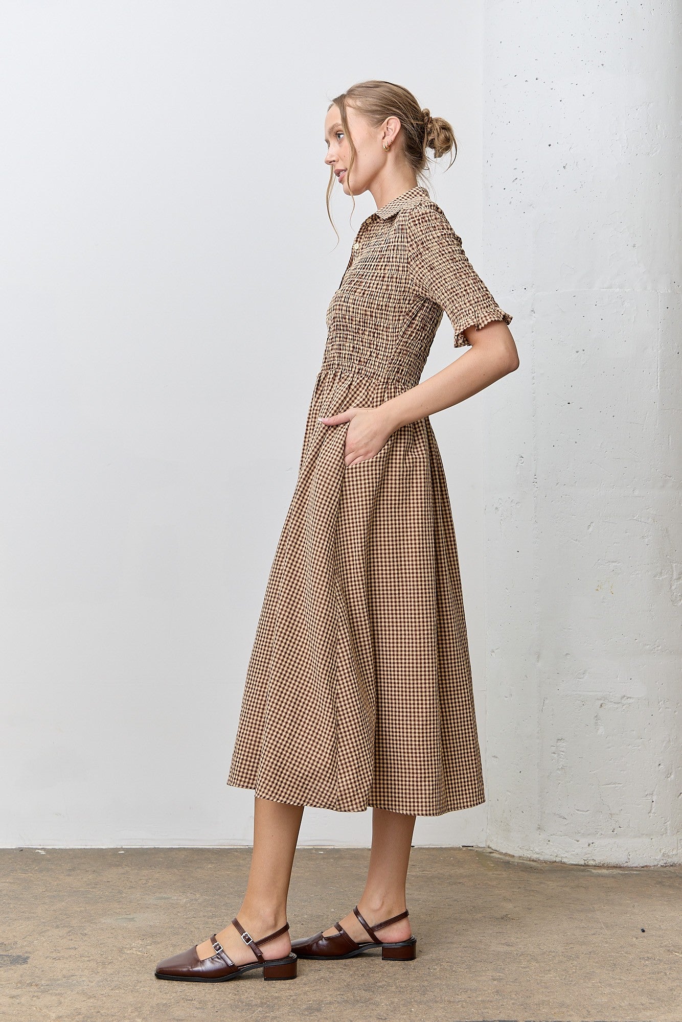 woman wearing a brown and cream checkered midi dress with a smocked bodice and pockets, styled with flat shoes