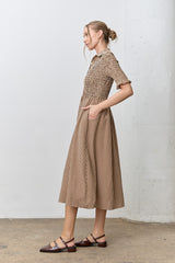 woman wearing a brown and cream checkered midi dress with a smocked bodice and pockets, styled with flat shoes