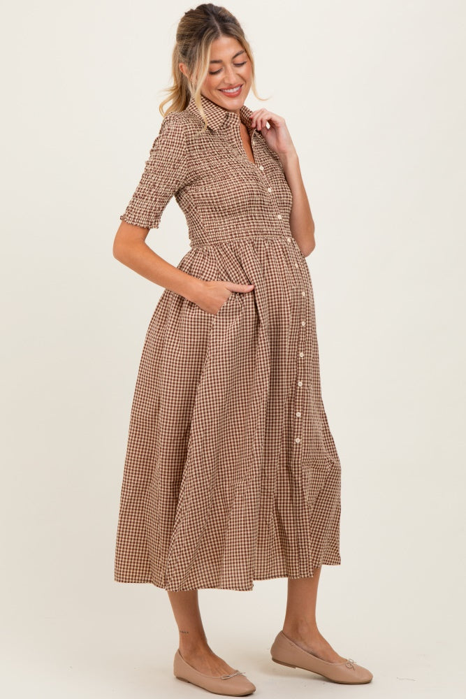 woman wearing a brown and white gingham maternity dress with short sleeves and pockets, highlighting her baby bump