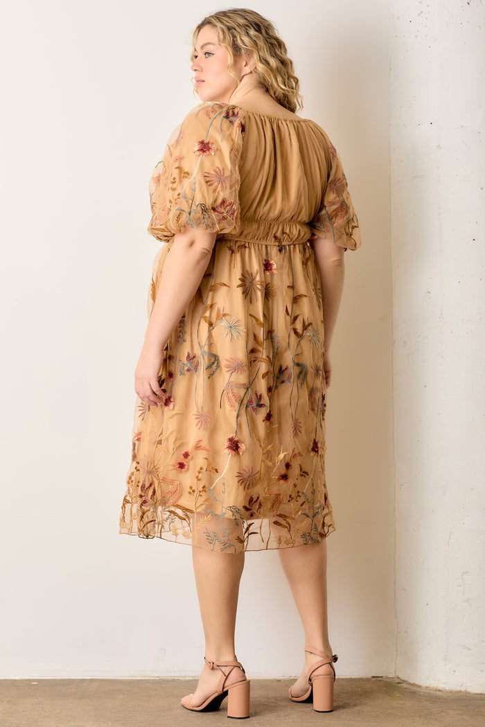 woman wearing a beige plus size dress with floral embroidery and puff sleeves, standing against a white wall