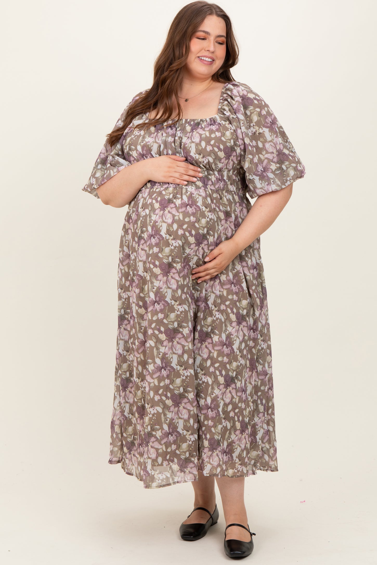 woman wearing a purple floral maternity dress with puff sleeves and a baby bump, smiling and holding her belly