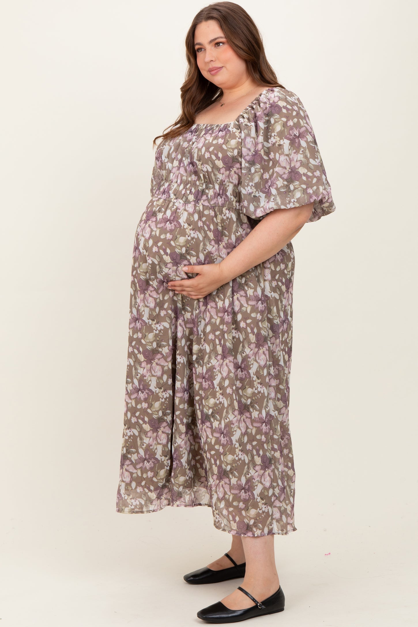 woman wearing a floral patterned maternity plus maxi dress, gently cradling her baby bump
