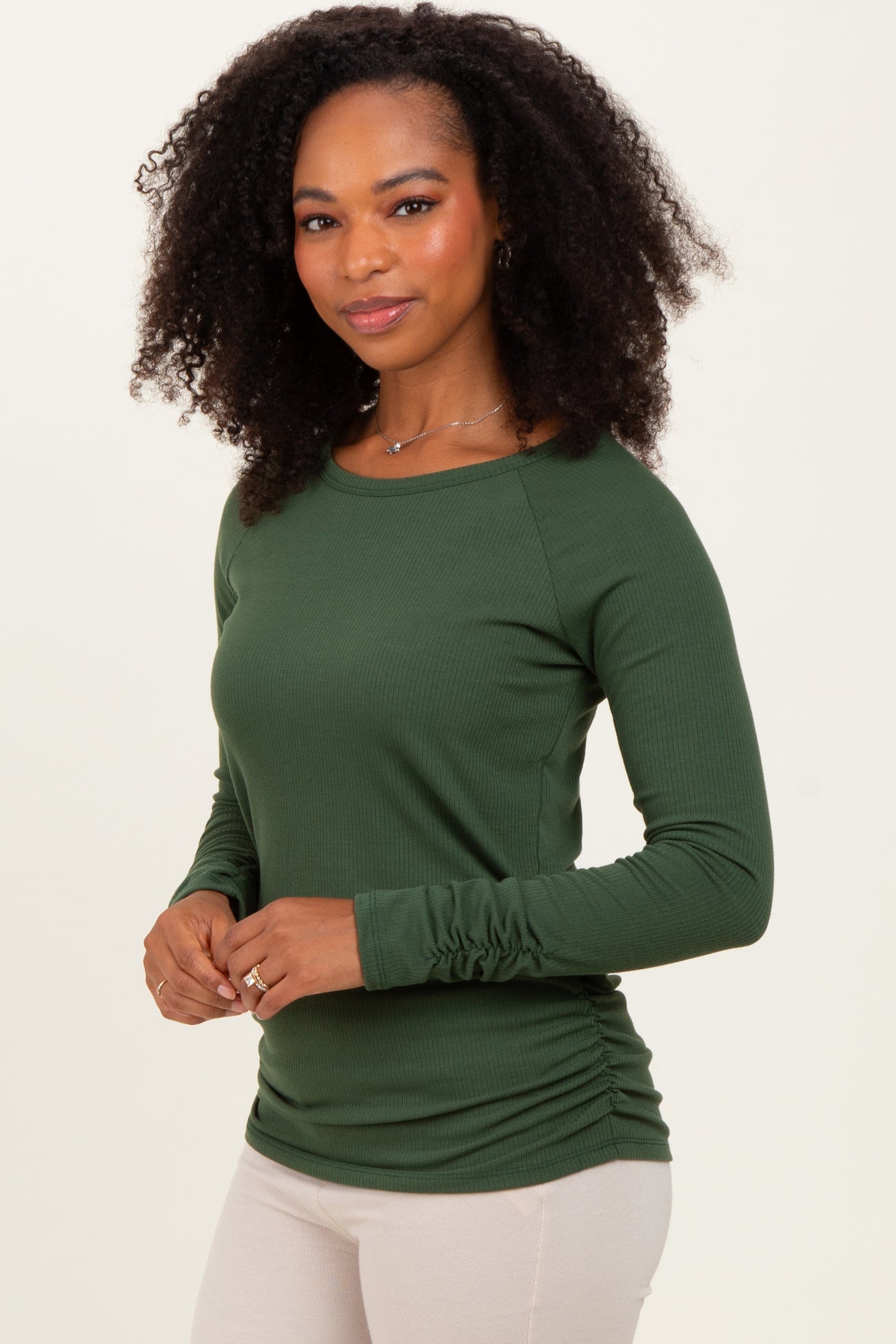 woman wearing a green long sleeve top with ruched sides and a round neckline