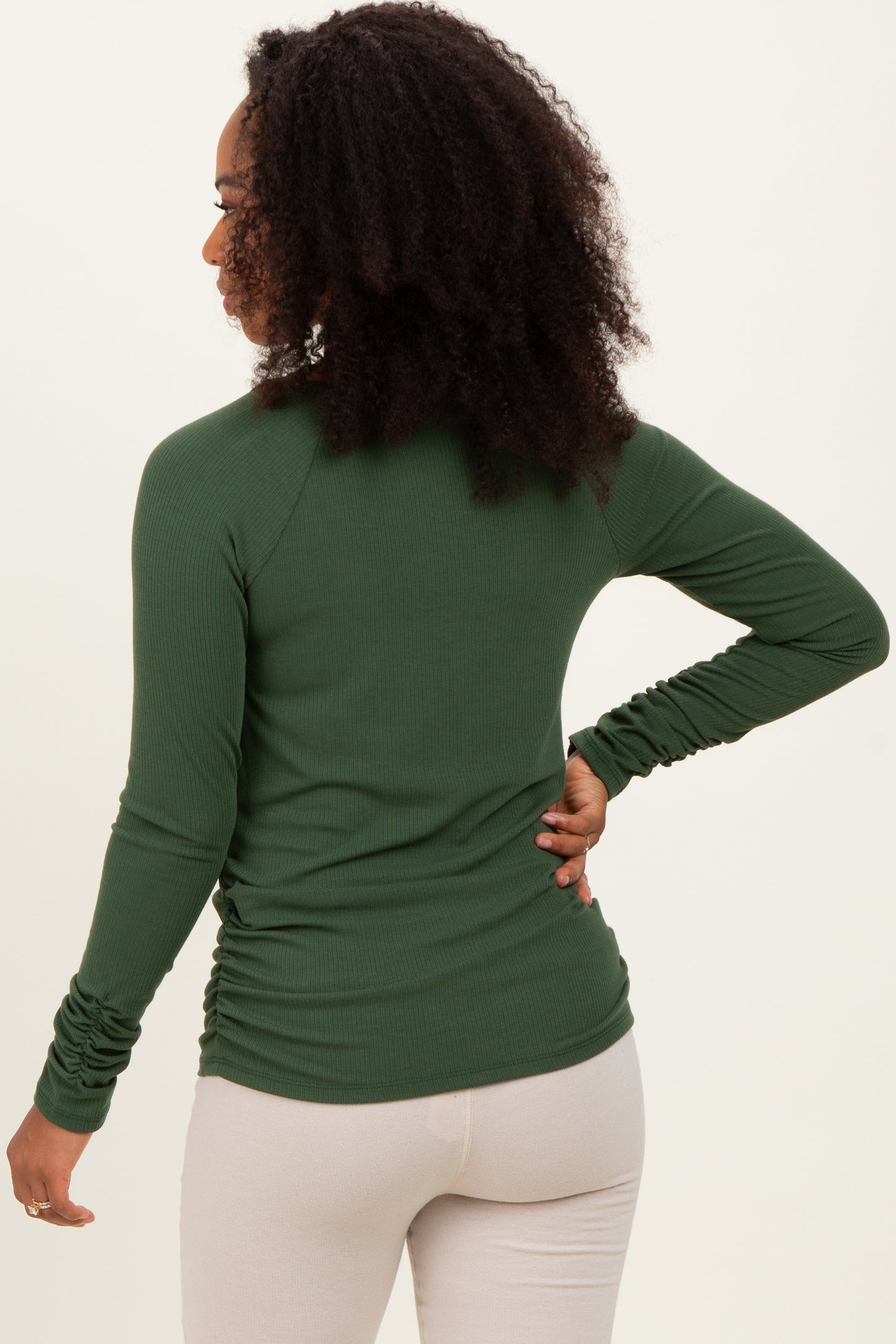 woman wearing a green long sleeve ribbed top with gathered side details, viewed from the back