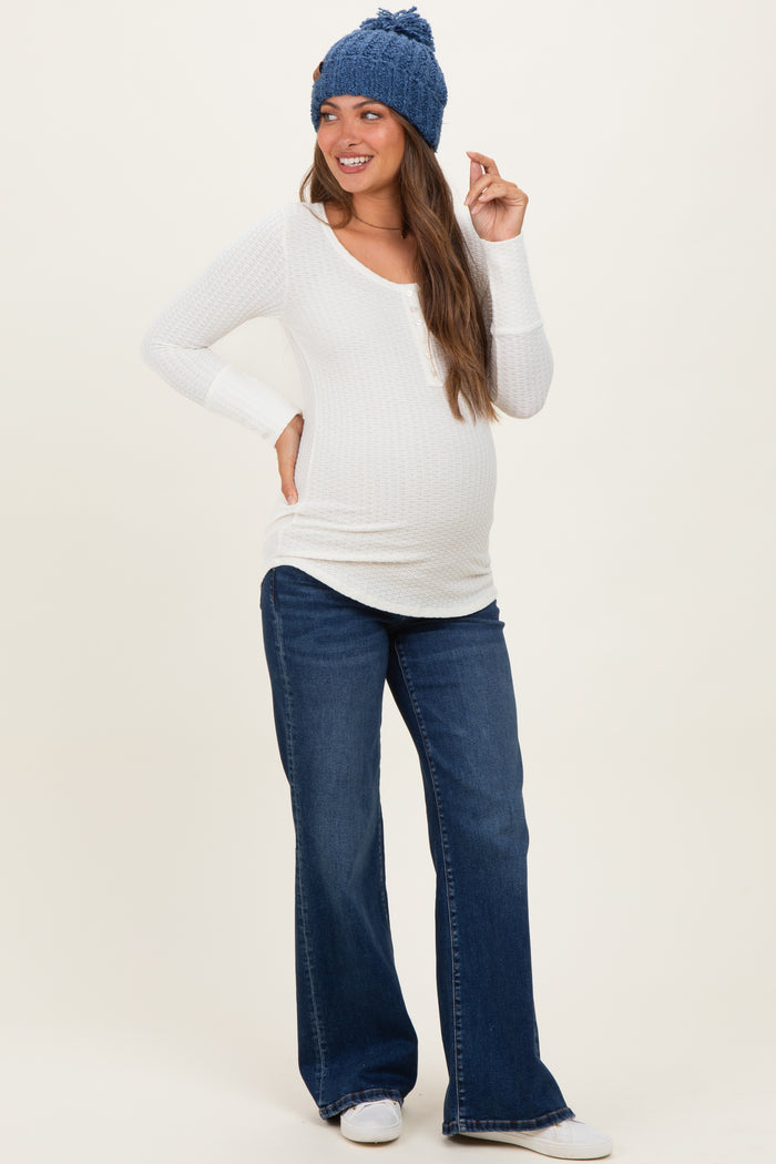 woman wearing a white long sleeve maternity top and blue flared jeans, showing her baby bump and smiling