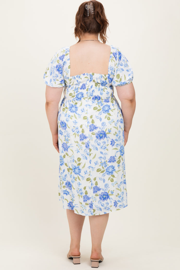 woman wearing a white floral maternity plus dress with blue and green flowers, showing a fitted back and puff sleeves