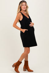 woman wearing a black maternity dress with pockets and a visible baby bump, paired with brown ankle boots