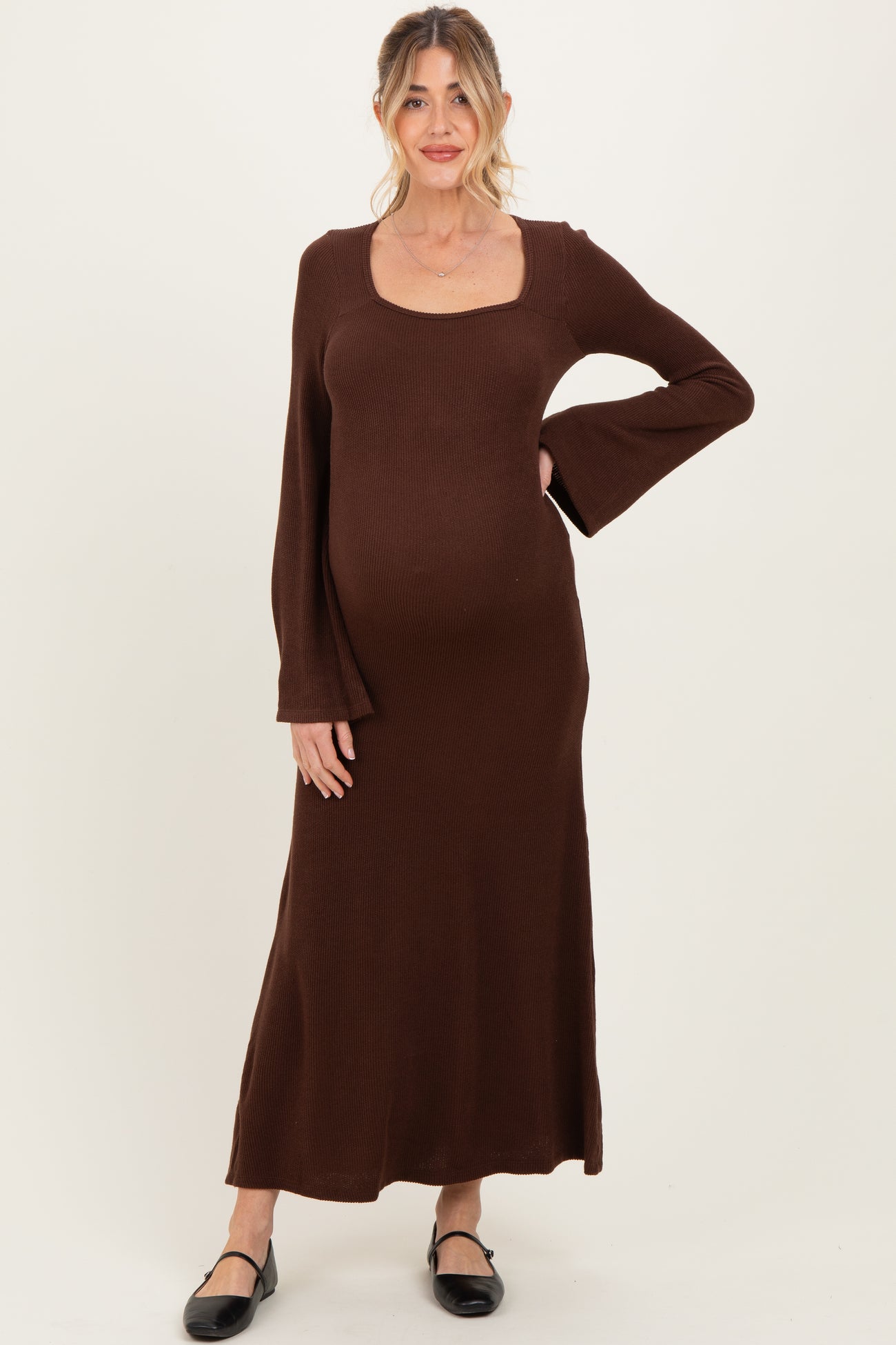 woman wearing a brown long sleeve maternity dress with a square neckline and flared sleeves, showcasing her baby bump