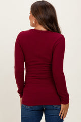 woman wearing a burgundy long sleeve maternity top, seen from the back, paired with blue jeans