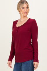 woman wearing a burgundy long sleeve henley top with button details and a scoop neckline, styled with blue jeans