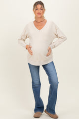 woman wearing a cream v-neck maternity sweatshirt with a front pocket and a visible baby bump, paired with blue jeans