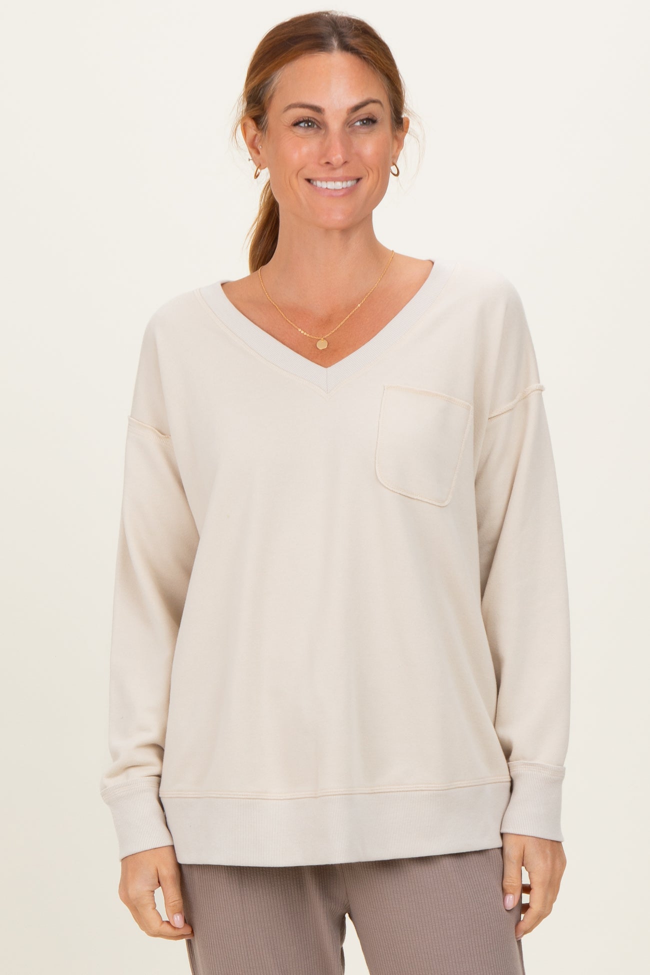 woman wearing a light beige oversized v-neck sweatshirt with a front pocket and relaxed fit