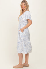 woman wearing a light blue floral midi dress with smocked bodice and short sleeves, standing with hands in pockets