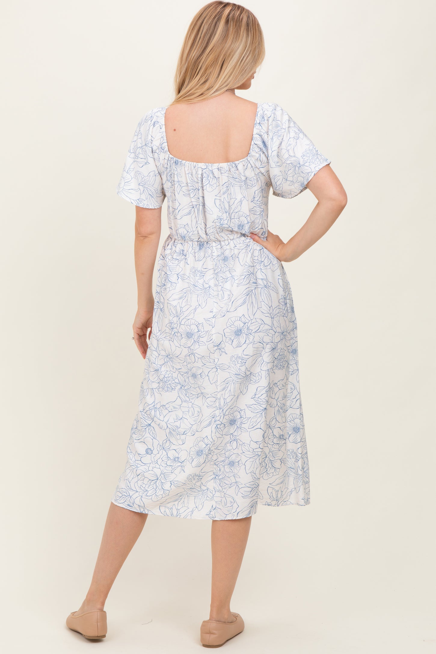 woman wearing a white floral print midi dress with short sleeves and a square back, standing with her back to the camera