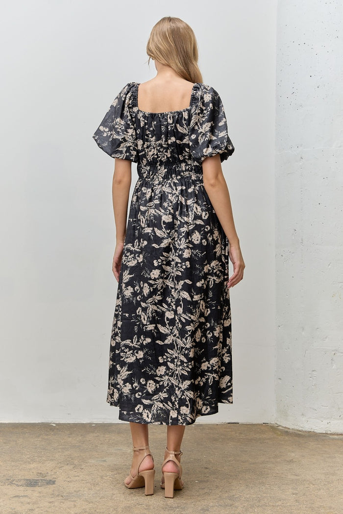 woman wearing a black floral maxi dress with puff sleeves and a smocked back, standing with her back to the camera