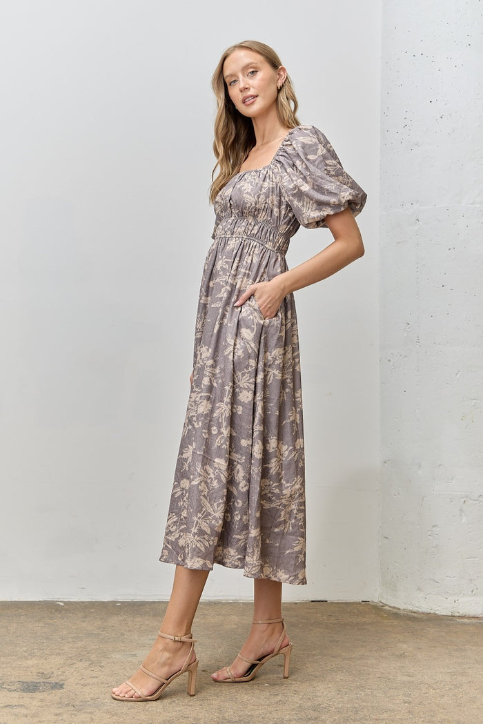 woman wearing a floral print midi dress with puff sleeves and pockets, standing in a neutral background