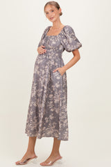 woman wearing a grey floral print maternity dress with puff sleeves and pockets, showing her baby bump