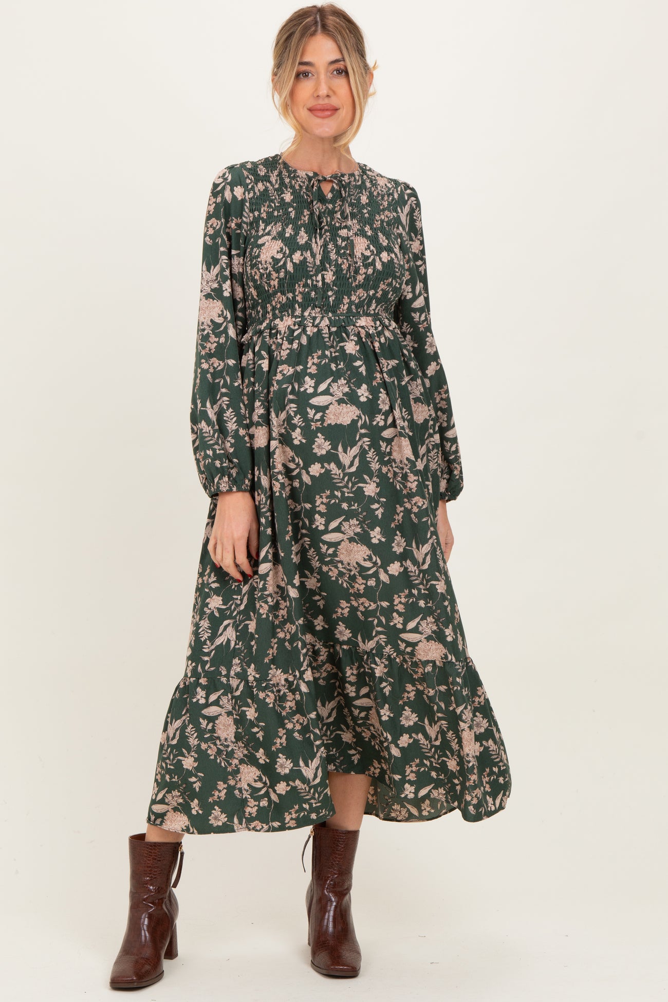 woman wearing a dark green floral print maternity dress with long sleeves and a fitted bodice showcasing her baby bump