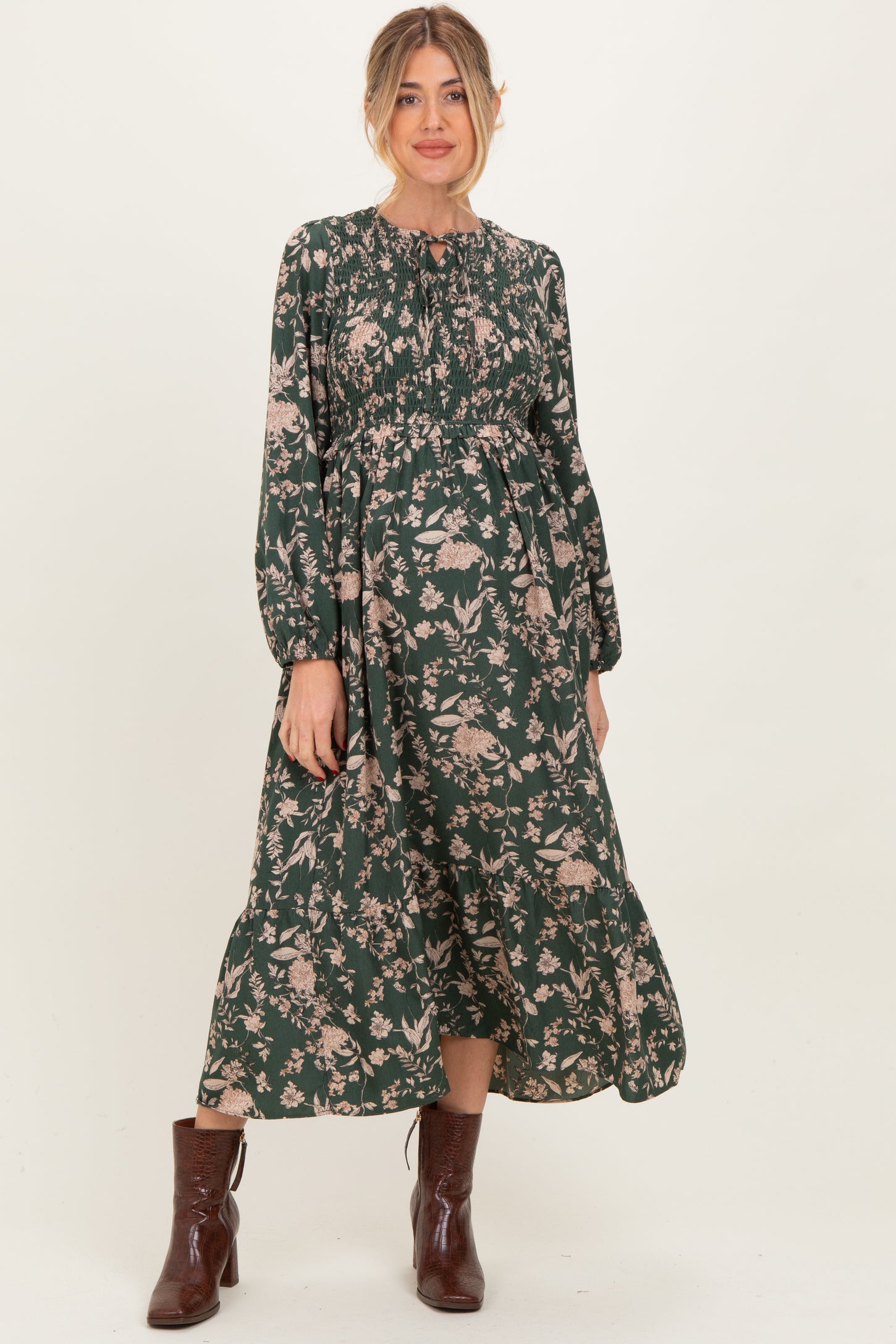 woman wearing a dark green floral print maternity dress with long sleeves and a fitted bodice showcasing her baby bump