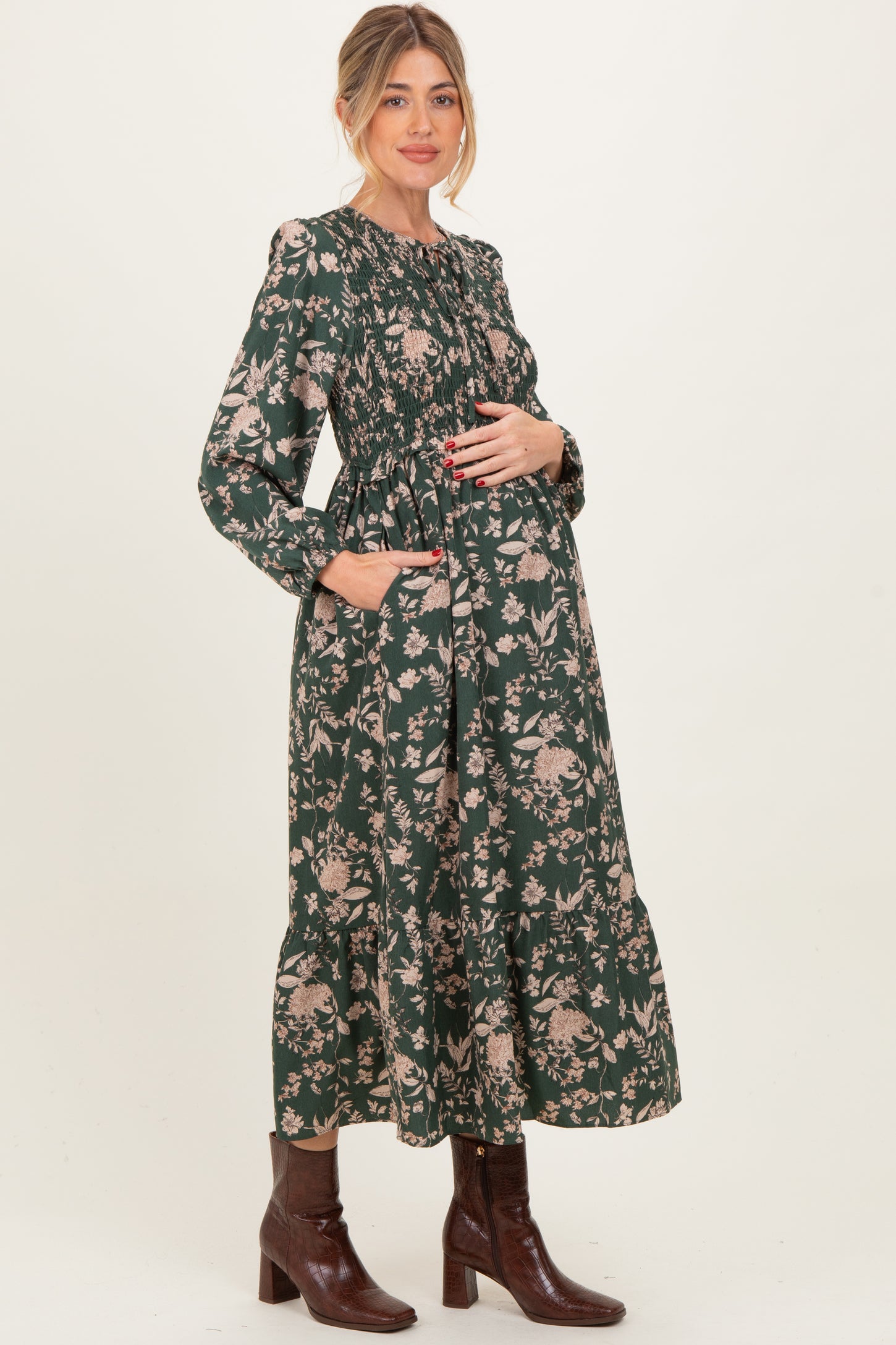 woman wearing a green floral maternity dress with long sleeves and a smocked bodice, holding her baby bump