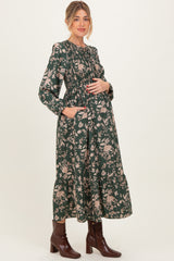 woman wearing a green floral maternity dress with long sleeves and a smocked bodice, holding her baby bump