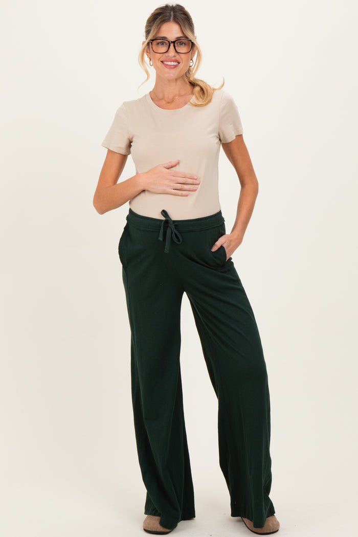 woman wearing a beige short sleeve top and green maternity loungewear pants with a visible baby bump
